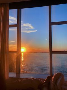 the sun is setting out over the ocean from a bedroom with large windows that look out onto the water