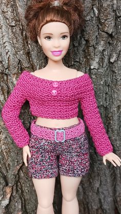 a doll is standing next to a tree wearing shorts and a pink sweater with buttons