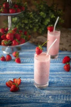 two glasses filled with strawberry milk and strawberries