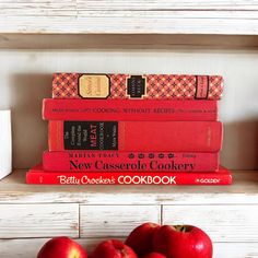 a stack of red books sitting on top of a white shelf next to some apples