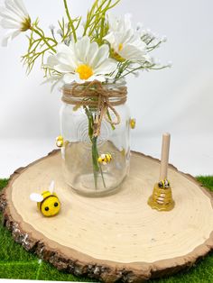 a mason jar filled with daisies sitting on top of a piece of wood next to a bee