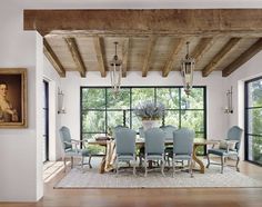 a dining room table with blue chairs in front of large windows and wooden beams on the ceiling