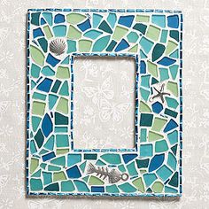 a blue and green mosaic light switch plate with sea shells on the bottom, in front of a wallpapered background