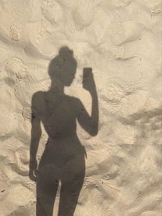 a shadow of a person holding a cell phone in front of a sand dune wall