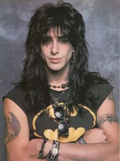 a man with long black hair wearing a batman shirt and ring on his left hand