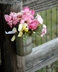 pink and yellow flowers in a tin can hanging on a fence