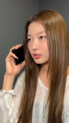 a woman with long brown hair holding a cell phone to her ear and looking at the camera