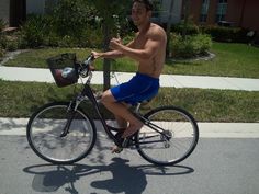 a shirtless man rides his bike down the street while giving thumbs up to someone