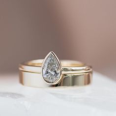 two gold wedding bands with a pear shaped diamond in the middle, on top of each other