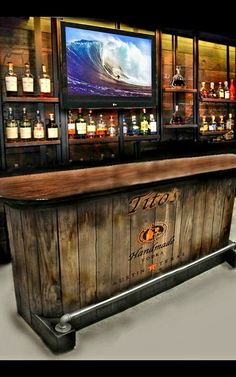 a wooden bar with bottles on the shelves and televisions above it in a room