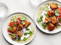 two white plates topped with tacos and vegetables