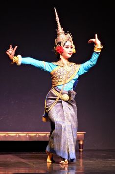 a woman is dancing on stage with her hands in the air and wearing an elaborate headdress