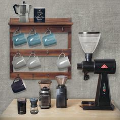 a coffee maker sitting on top of a wooden table next to cups and mugs