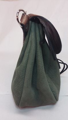 a green bag with a metal ring on the bottom and a black leather handle hanging from it