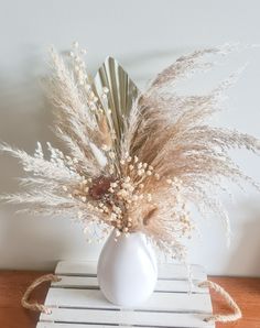 a white vase filled with dried flowers on top of a wooden table