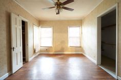 an empty room with two windows and a ceiling fan