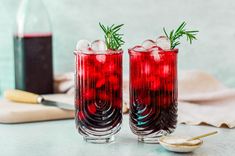 two glasses filled with red liquid and garnished with rosemary