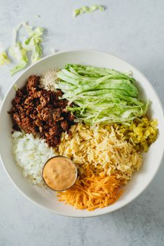 a white bowl filled with rice, meat and veggies on top of a table