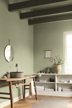 a bathroom with green walls and wooden flooring next to a white shelf filled with towels