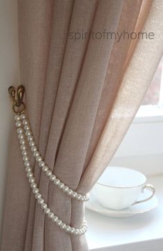 a curtain with pearls hanging on it next to a cup and saucer in front of a window