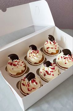 six cupcakes with white frosting and oreo cookies in a cardboard box