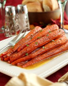 there are carrots on the white plate and silverware next to some bread rolls