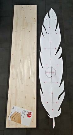 a large white feather sitting next to a piece of plywood board on the floor