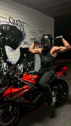 a man sitting on top of a red motorcycle in front of a graffiti covered wall