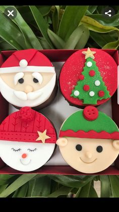 four decorated cupcakes in a red box on top of a table next to plants