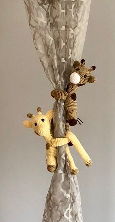 two stuffed giraffes are hanging from a curtain with white and gray fabric