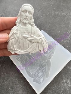 a hand holding a plastic stamp that has a statue of jesus on it