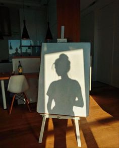 a shadow of a woman is on an easel in the middle of a room