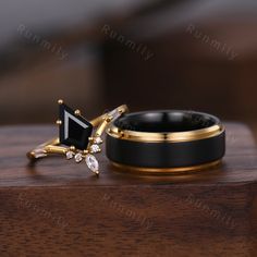 two wedding rings with black and gold accents sit on a wooden table next to each other