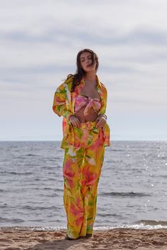 a woman standing on top of a sandy beach next to the ocean with her hands in her pockets