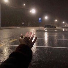 someone is holding their hand out in the rain at night on an empty parking lot