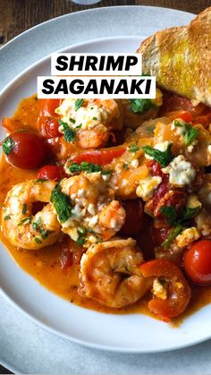 a white plate topped with shrimp and tomato stew next to a piece of bread on top of a wooden table