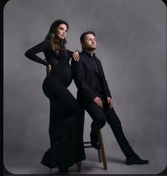 a pregnant woman sitting on top of a stool next to a man in a suit