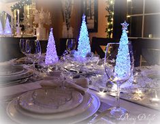 a dining room table set for christmas with blue and white lights on the tree centerpieces