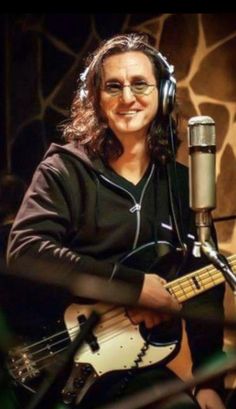 a man sitting in front of a microphone while holding a guitar and wearing headphones