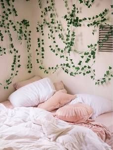 an unmade bed with white sheets and pink pillows in front of ivy covered wall