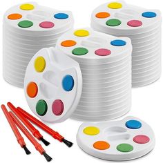 a group of paint brushes and paints on top of some white plates with different colors