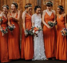 a group of women standing next to each other wearing orange dresses and holding bouquets