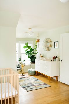 a baby's room with a crib, dresser and plant in the corner