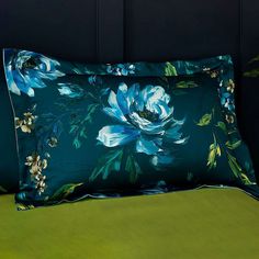 a blue flowered pillow sitting on top of a green bed cover next to a black headboard