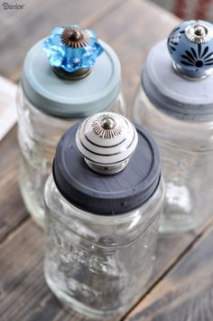 three glass jars with lids and knobs on top of a wooden table next to each other