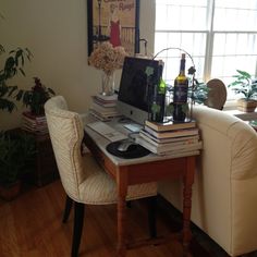 there is a desk with books and bottles on it in front of the window, along with two chairs