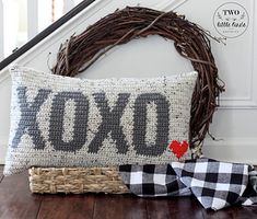 a cross stitch pillow sitting on top of a wooden floor next to a basket with a red heart