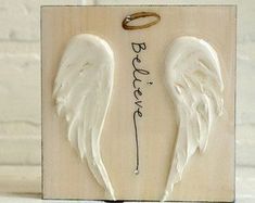 two white angel wings with the word peace on them are attached to a wooden plaque