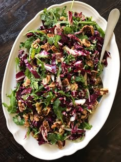 a white plate topped with a salad on top of a wooden table next to a fork