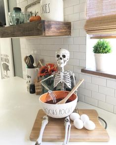 a fake skeleton in a bowl with eggs on a cutting board next to some utensils